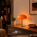 Lampe de table dôme orange, base chromée, posée sur un meuble en bois