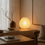 Lampe Wabi globe en fibres claires, trépied doré, posée près d’un vase