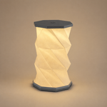 Lampe plissée nomade, abat-jour beige plié en relief, base hexagonale grise, capot noir