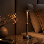 Lampe Flambeau sur table, pied noir et tige dorée, abat-jour rond sombre.