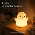 Veilleuse manchot allumée, silhouette blanche aux ailes courtes, bec jaune.