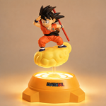 Figurine lumineuse de Goku sur nuage jaune, pose accroupie, baguette rouge, base orange.
