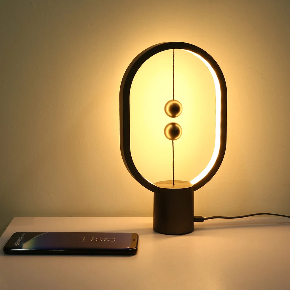 Lampe à équilibre magnétique ovale noire, deux boules cuivre suspendues, lumière chaude.