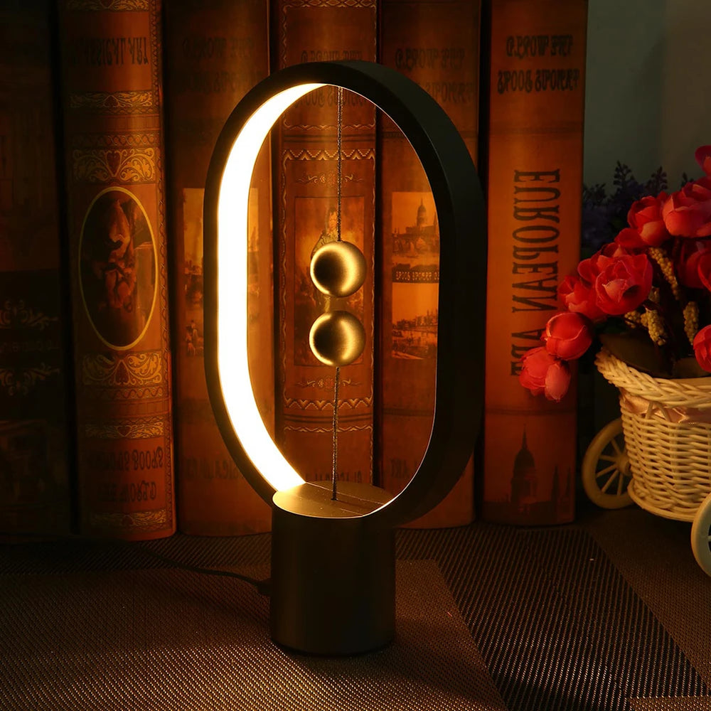 Lampe à équilibre magnétique avec éclairage en anneau ovale noir et deux boules cuivre.