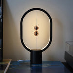 Lampe à équilibre magnétique : anneau ovale noir, tiges verticales et deux boules cuivre.