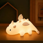 Veilleuse dragonnet en silicone blanc, lumière chaude, vue de profil sur meuble.